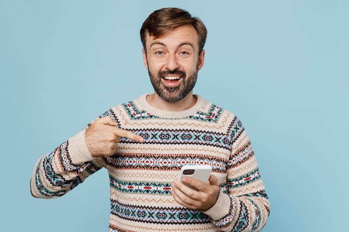 Homme en pull d'hiver montre son smartphone, hyper content avec les 130 Go de Cdiscount Mobile