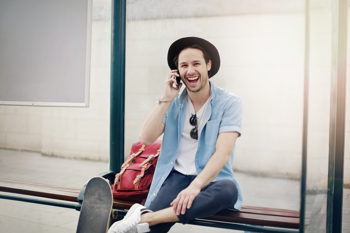 Homme tout sourire à l'arrêt de bus car il téléphone pas cher sur réseau Bouygues Telecom avec Lyca Mobile