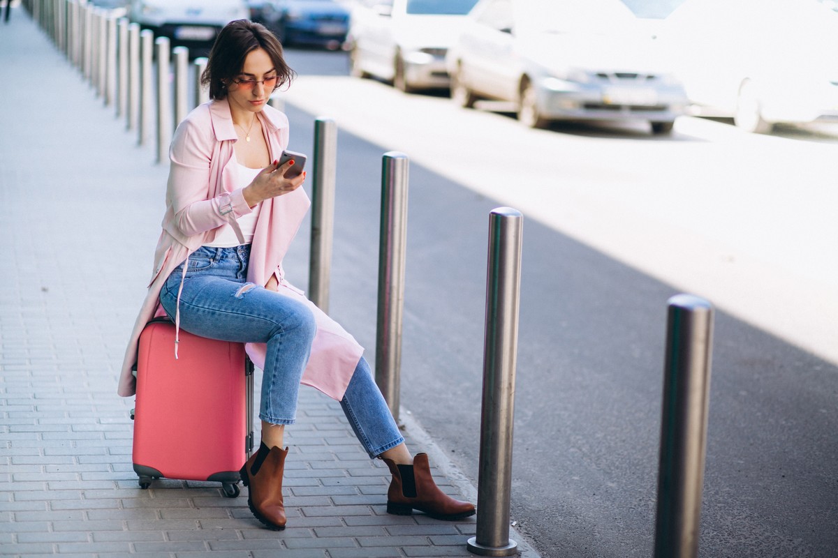 Femme assise sur sa valise, et un smartphone pour téléphoner à l'étranger gratuit avec Réglo Mobile