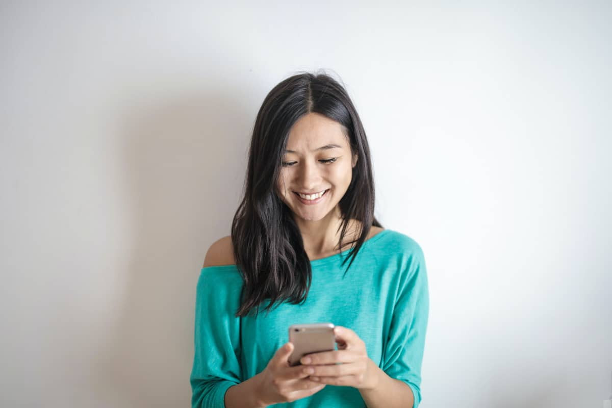 Femme sourit avec son smartphone, car forfait mobile de Lebara sur le réseau d'Orange