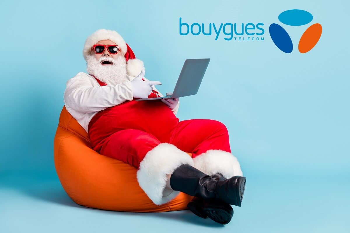 Père Noël avec lunettes de soleil et PC portable, très souriant grâce à 2 mois d'abonnement gratuit chez Bouygues Telecom