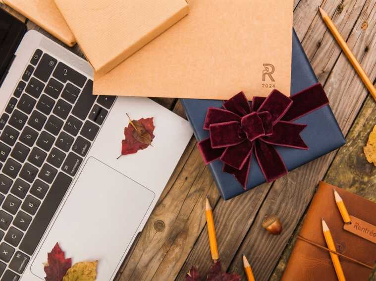 Ordinateur, cahiers, crayons et cadeau bleu avec ruban bordeaux sur une table en bois avec des feuilles d'automne.