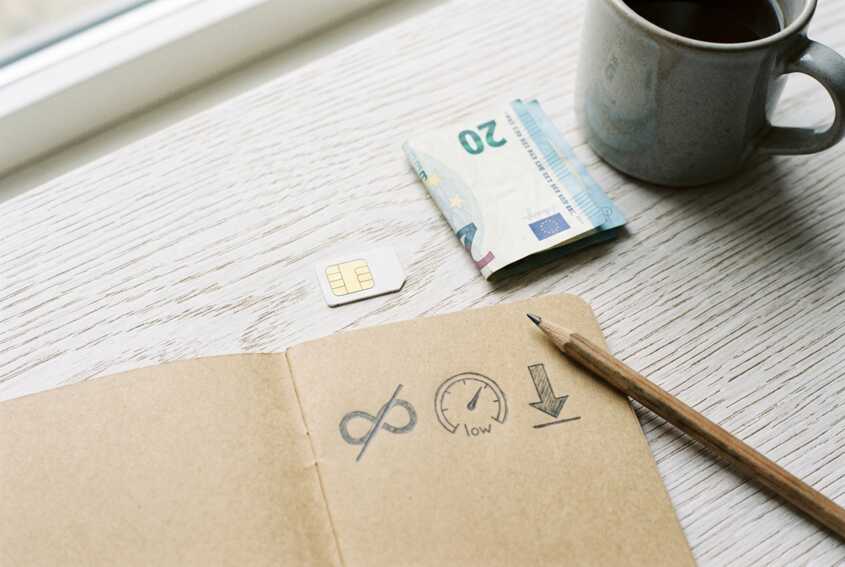 Carte SIM, billet, carnet avec icônes data, crayon et mug sur fond en bois clair.