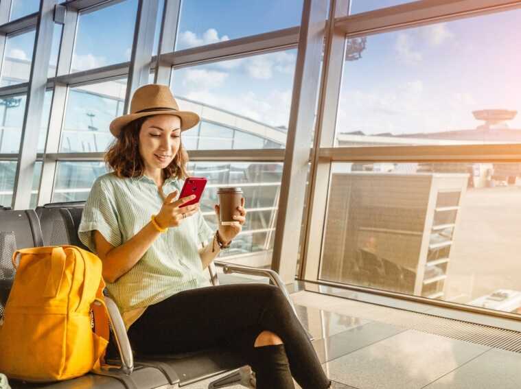 Femme regarde son smartphone à l'aéroport, et fais le nécessaire pour diminuer sa consommation mobile