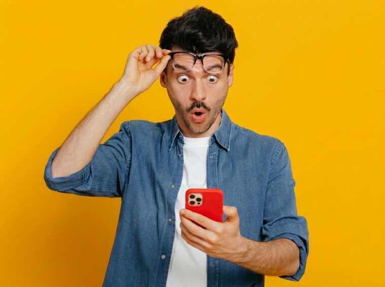 Homme lève ses lunettes de surprise en regardant son smartphone, épaté par les 350Go de 5G et ouverture sur l'international du forfait XXL de Syma