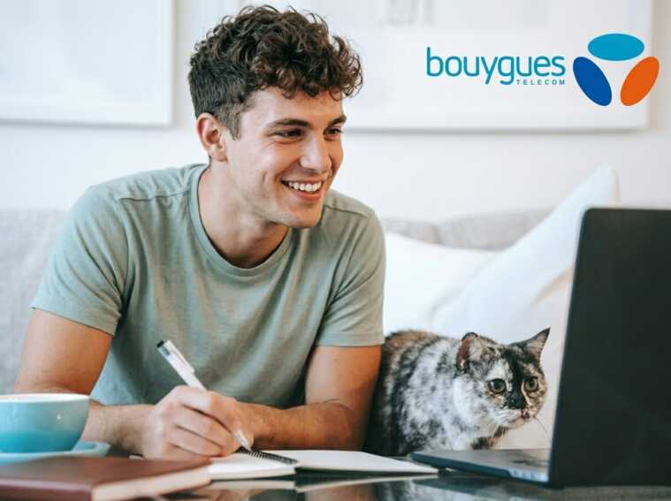 Jeune homme brun travaillant sur un ordinateur portable avec un chat à ses côtés, logo Bouygues Telecom.