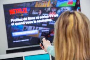 Femme streame Netflix sur télé, car la plateforme voudrait racheter son concurrent Warner Bros. Discovery