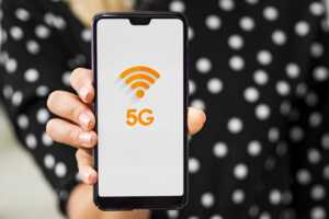 Main de femme montre smartphone avec logo 5G couleur orange, car baisse de prix sur la 5G d'Orange chez YouPrice