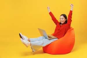 Femme assise sur pouf avec PC portable lève les bras en signe de victoire, ravie de la série spéciale "Livebox Lite Fibre"