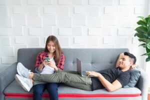 Couple dans canapé, avec PC portable et smartphone, utilise le Wi-Fi, qui fête ses 25 ans