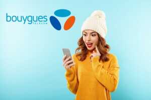 Femme à bonnet et pull jaune et logo de Bouygues Telecom derrière, épatée par son nouveau smartphone pas cher car remises jusque 300€ avec un forfait