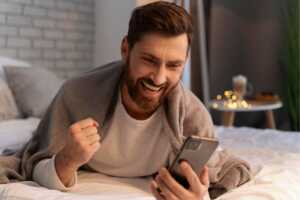 Homme dans son lit avec smartphone, content de 3€ de remise sur forfait mobile en combo avec Bbox B&YOU