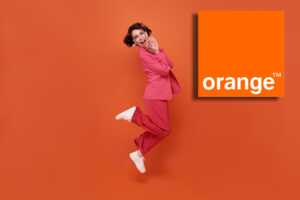 Femme en tailleur rose sur fond Orange saute de joie devant logo d'Orange, car Série Spéciale Fibre à prix fixe