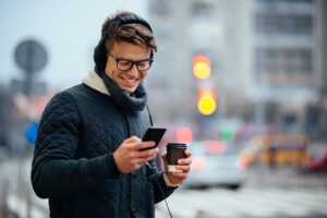 Homme avec smartphone et café dans les mains sourit, ravi de son forfait Sosh de 90 Go à moins de 8€ pour le Black Friday
