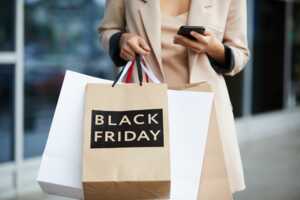 Femme tient smartphone et sacs shopping "Black Friday" dans les mains avec iPhone 16 à petit prix de chez Rakuten