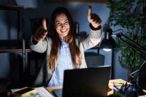Femme devant PC lève les pouces et sourit, heureuse d'avoir pu choisir un abonnement Internet à prix fixe