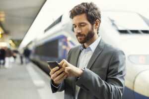 Un commercial regarde son smartphone sur le quai d'une gare TGV