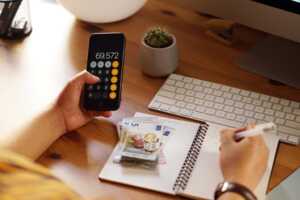 Main d'homme avec calculatrice, carnet de note et pile de pièces et billets, vérifie que souscrire chez Bouygues Telecom ne co^te rien grâce aux frais de mise en service offerts