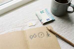 Carte SIM, billet, carnet avec icônes data, crayon et mug sur fond en bois clair.