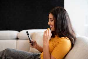 Femme sur canapé avec smartphone, regarde TV via l'application OQEE avec forfait mobile de Free