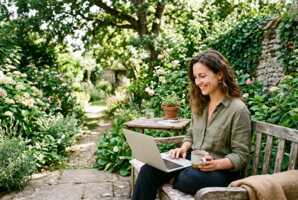 Une femme assise dans un jardin regarde une série sur son ordinateur portable.