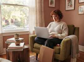 Une femme assise dans un fauteuil utilise un ordinateur portable sans logo sur le capot.