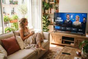 Une femme regarde la télévision dans un salon éclairé par la lumière du jour.