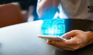 Femme tient smartphone avec logo 5G au laser bleu, car Coriolis offre un forfait compatible à moins de 7€ avec déjà 40Go,