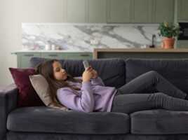 Une jeune fille allongée sur un canapé gris utilise un smartphone grâce à B&YOU