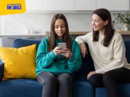 Une adolescente utilise un smartphone sur un canapé bleu à côté de sa mère.
