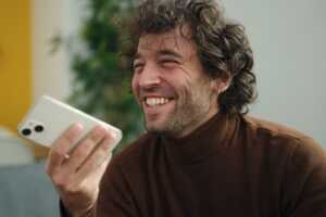 Homme avec smartphone fait un grand sourire, ravi de payer 3€ moins cher son forfait mobile car abonné à la Box "Pure Fibre" de B&YOU