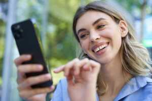Femme sourit en regardant son smartphone, ravie des ses 60Go de 5G à moins de 5€, prix réduit car abonnée RED Box