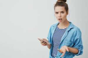 Femme avec smartphone à la main, déçue car le marché des forfaits mobile a augmenté de 17.4% en un an, et rien ne se passe depuis janvier car vente SFR en cours