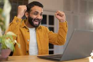 Homme en chemise orange lève les bras de joie, ravi de ses équipements offerts avec sa Box