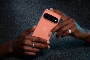 Mains tenant un smartphone Google Pixel rose sur un fond gris texturé.