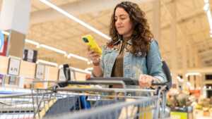 Femme avec smartphone pousse caddie dans supermarché, car Lidl va bientôt lancer sa gamme de forfaits mobile