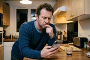 Un homme mécontent regarde son téléphone portable dans une cuisine.