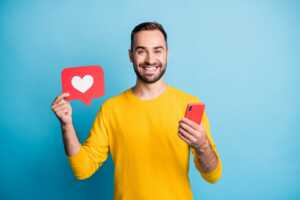 Homme en t-shirt jaune avec smartphone dans la main et coeur like, ravi de son Galaxy A16 à moins de 130€ avec un forfait 4G pas cher