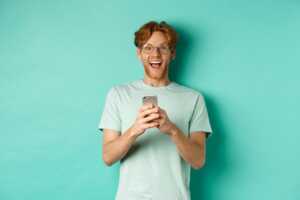 Homme sur fond vert avec smartphone, heureux des prix fous chez YouPrice