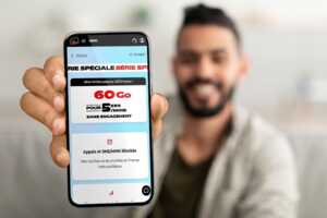 Homme souriant montre son iPhone, avec pub pour forfait de 60Go à moins de 6€ grâce à la vente privée entre Ariase et NRJ Mobile