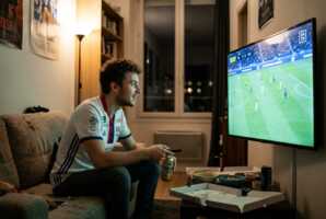 Un jeune homme regarde un match de football sur un téléviseur diffusant via DAZN.