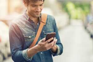 Homme regarde son téléphone et sourit, content avec nouveau forfait 50 Go de Cdiscount Mobile