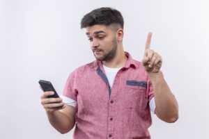 Homme doigt levé regarde son smartphone, pour faire attention à 5 détails importants de son forfait mobile