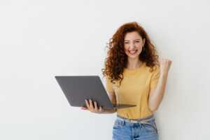 Jeune femme avec PC portable sourit de toutes ses dents car elle a une Box Internet à prix réduit car elle a moins de 26 ans