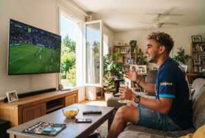 Un jeune homme regarde un match de football à la télévision sur Canal+ en été.
