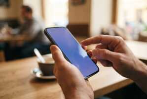 Gros plan sur des mains tenant un smartphone avec un écran bleu-violet, doigt prêt à toucher l'écran.