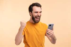Homme serre le poing en signe de joie devant son smartphone, ravi du nouveau forfait YouPrice avec 200Go de 5G sur réseau Bouygues Telecom à moins de 9€