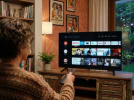 Une personne de dos utilise une télécommande devant un téléviseur affichant l'interface d'accueil Android TV.