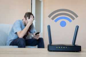 Homme avec smartphone, tête dans la main, et Box Internet au 1er plan avec logo Wi-Fi, car comment améliorer la connexion sans fil ?