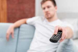 Homme avec télécommande zappe dans son canapé, ravi des 3 nouvelles chaînes offertes avec sa Livebox d'Orange